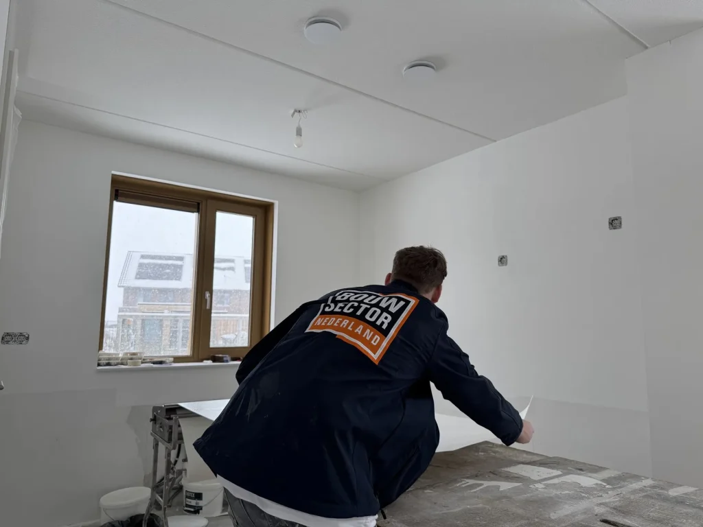Behanger van Bouwsector Nederland in donkere werkjas pakt een baan vlies van de plaktafel