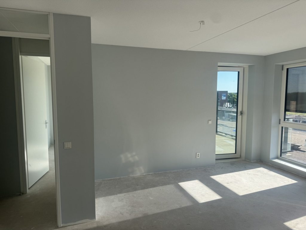 Kamer in een appartement met een balkondeur en een lichtgrijs afgewerkte wand