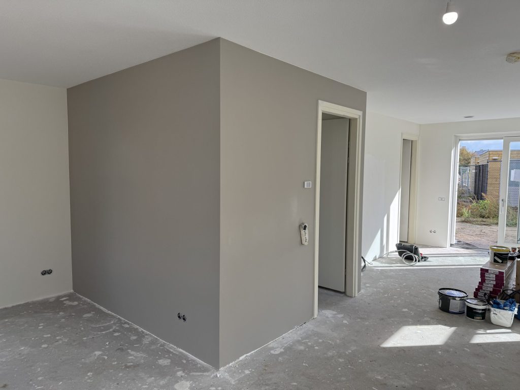 Pas afgewerkte grijze wand in een woonkamer met verfemmers op de vloer