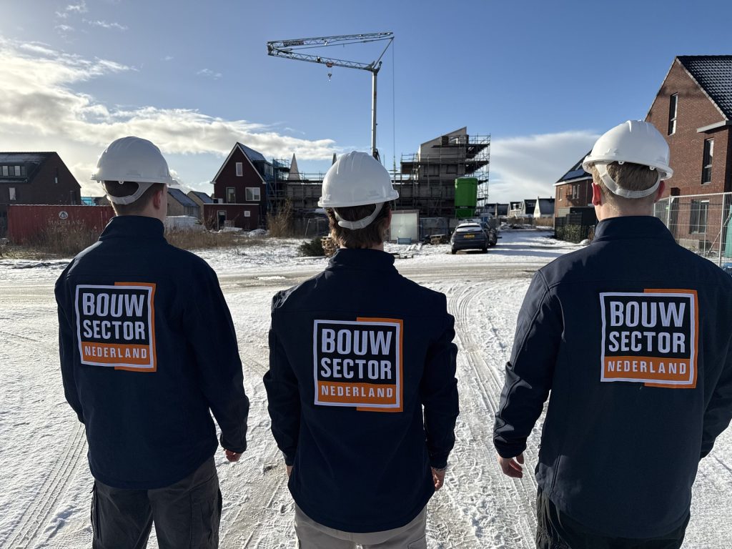 Drie vakmensen van Bouwsector Nederland met witte helm op een besneeuwde bouwplaats